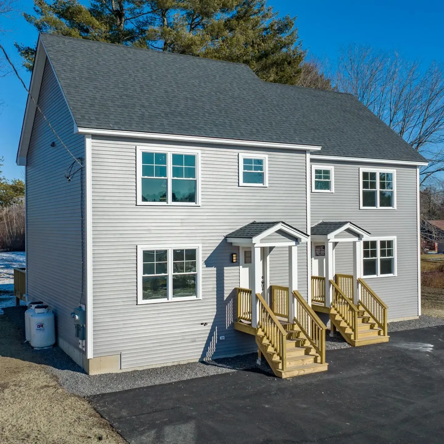 A gray clapboard duplex with crisp white trim and new entry stairs, bare trees and snow still on the ground
