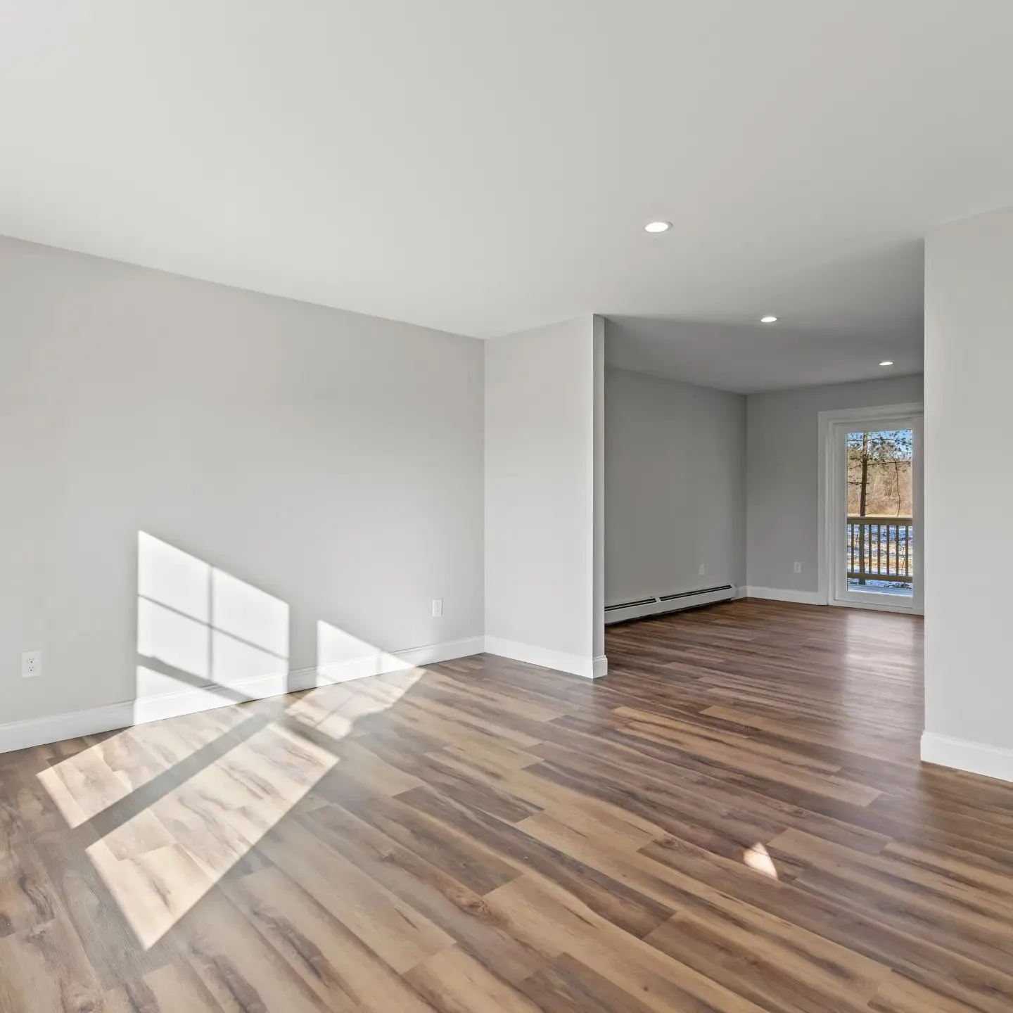 Freshly painted living room with pale grey walls, crisp white baseboards, and afternoon light across the wood floor